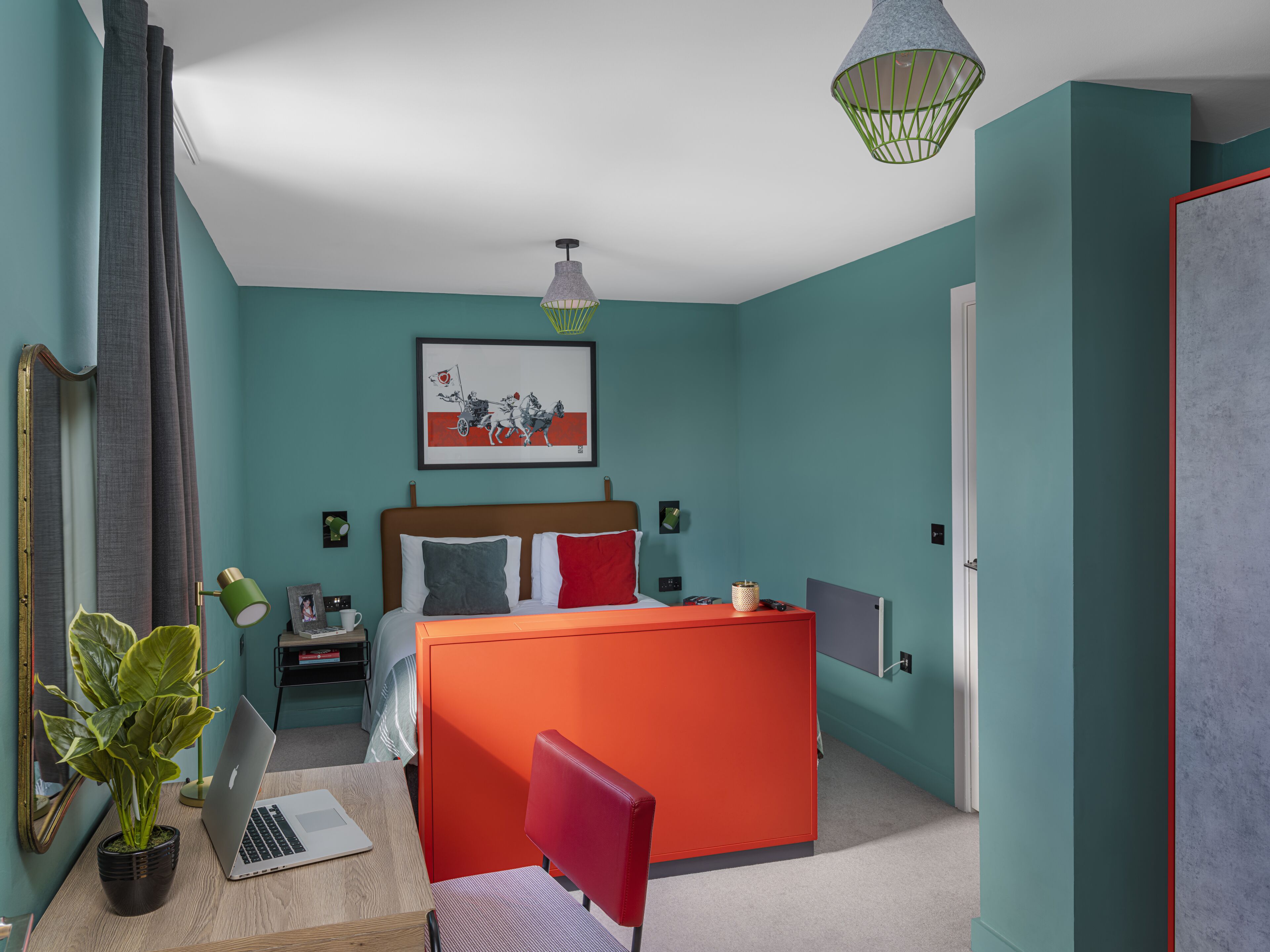 A modern bedroom with teal walls, a wooden bed, a red desk, and a laptop.