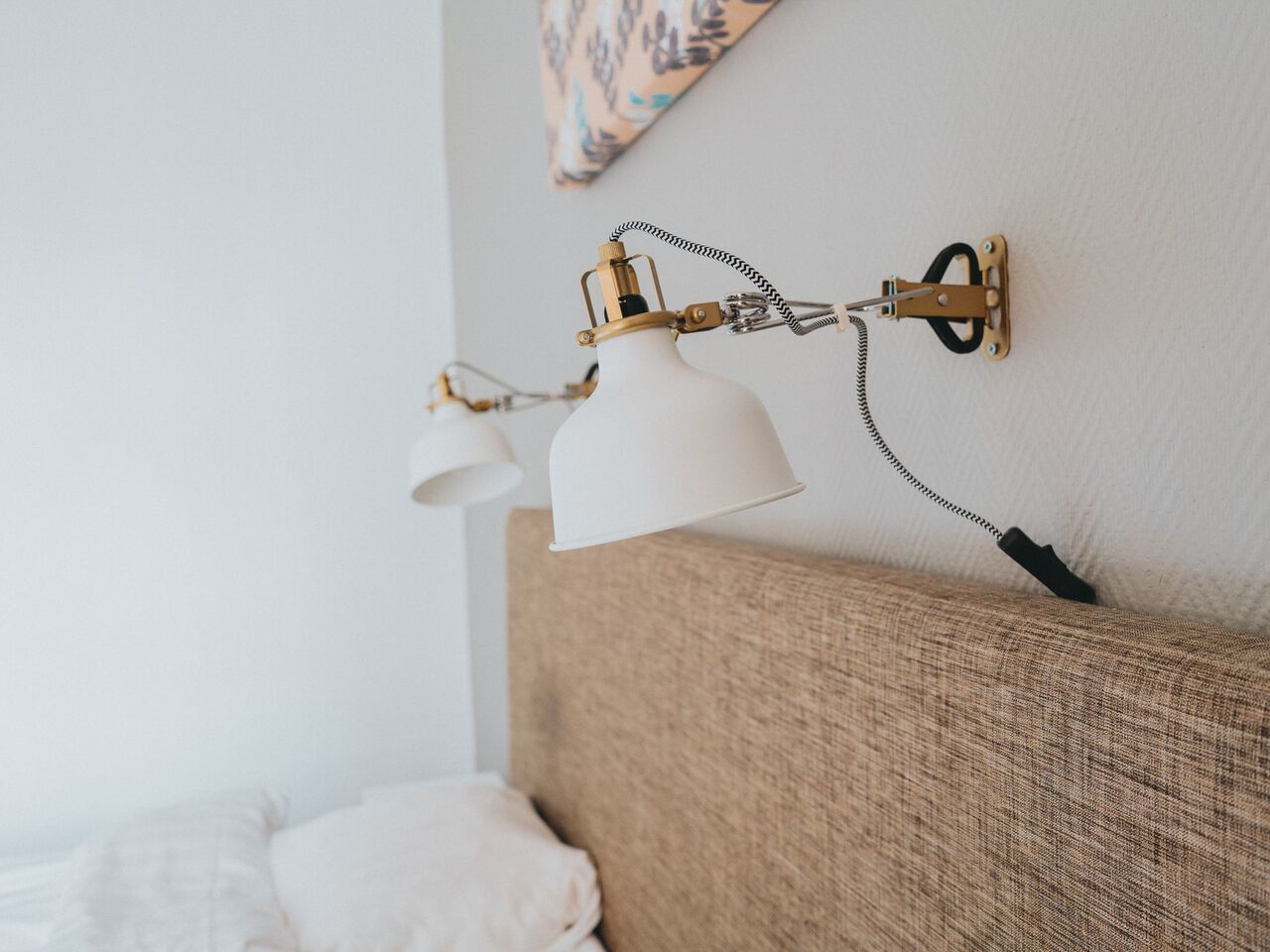 A wall-mounted lamp with a white shade and a brass fixture against a textured wall.