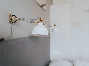 Una habitación moderna con cabecera gris, lámpara de noche blanca y armario blanco.