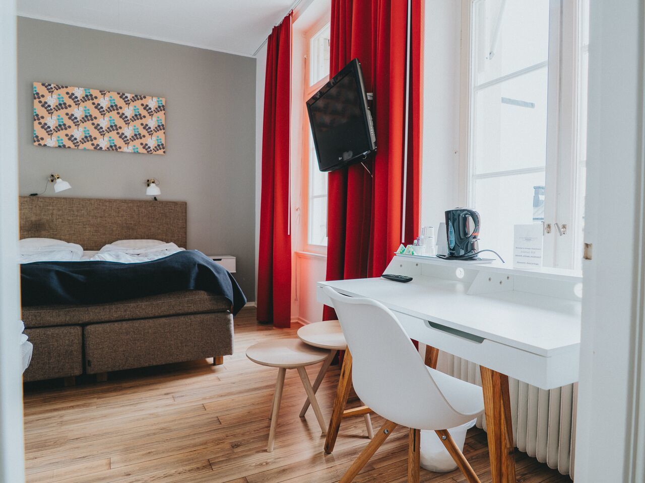 Une chambre à coucher avec un lit, un bureau, une chaise, un téléviseur et une fenêtre avec des rideaux.