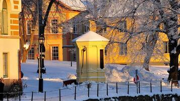 A snow-covered outdoor area with a stone wall, a small yellow structure, and buildings in the background.