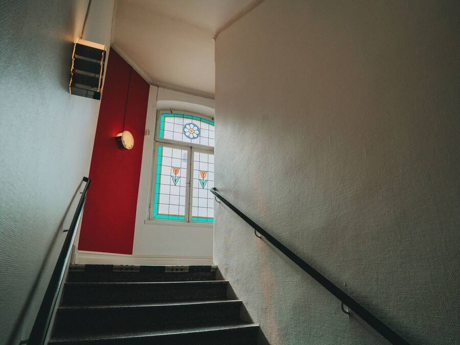 Una escalera con una pared roja y una ventana con un diseño floral.