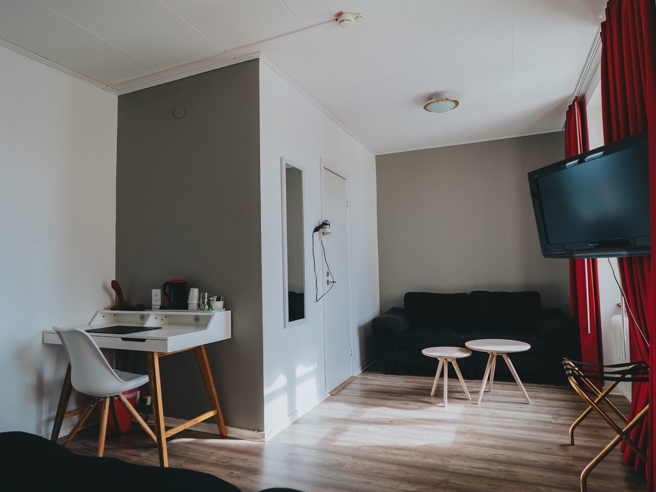 A compact living space with a kitchenette, a dining area with two stools, a sofa, and a TV mounted on the wall.