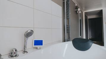 A modern bathroom with a white bathtub, a digital shower control panel, and a chrome faucet.