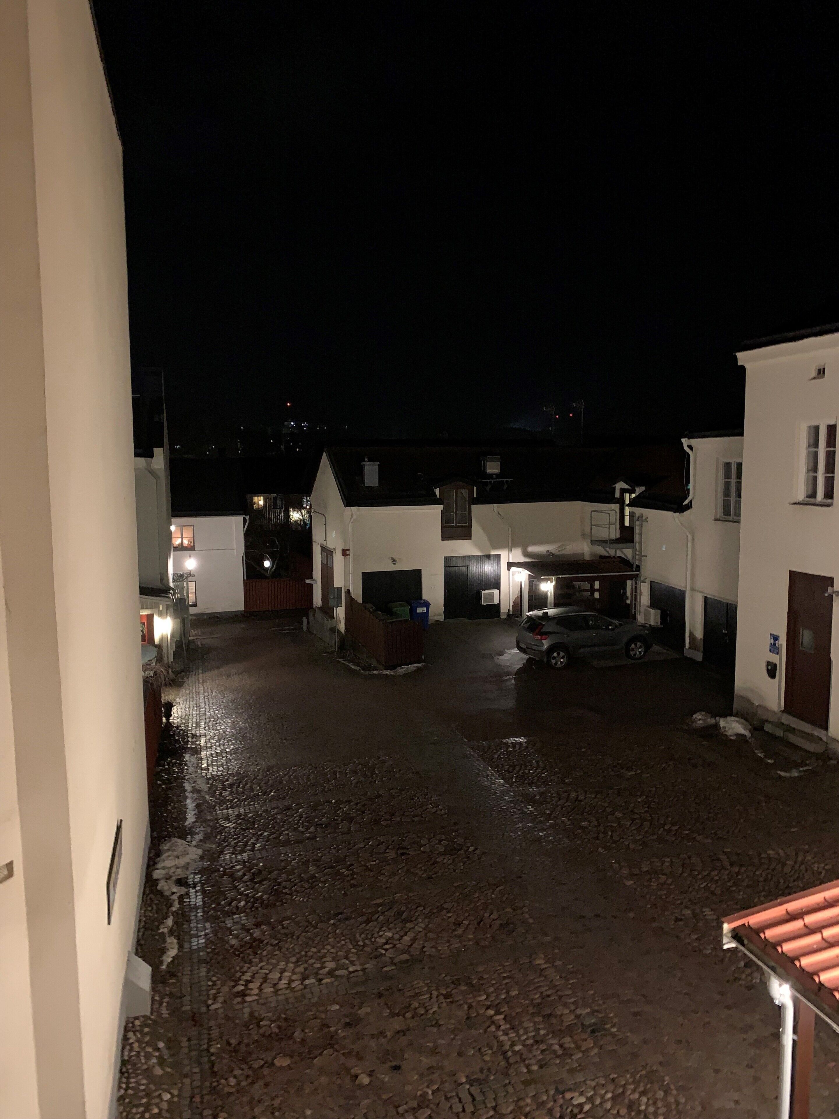 Un patio con suelo de adoquines, edificios blancos y un coche estacionado.