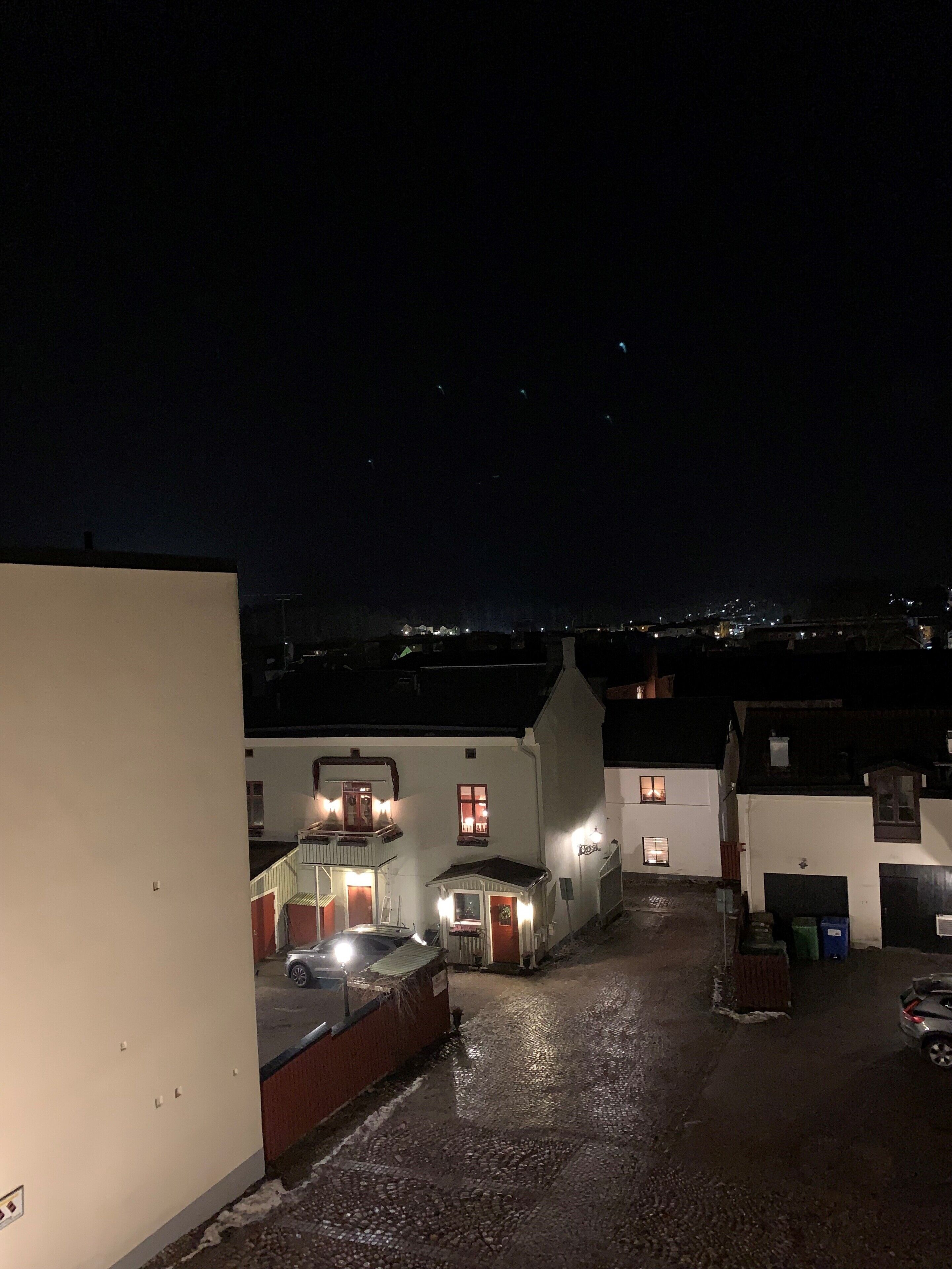 Vista nocturna de una zona residencial con casas, un camino de entrada pavimentado y un coche estacionado en primer plano.