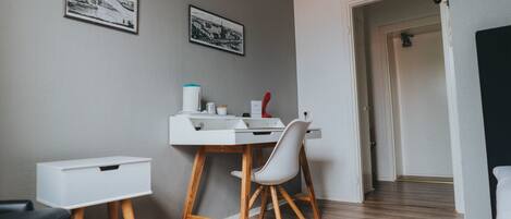 A modern room with a white desk, chair, and storage unit. There are two framed pictures on the wall and a door leading to another room.