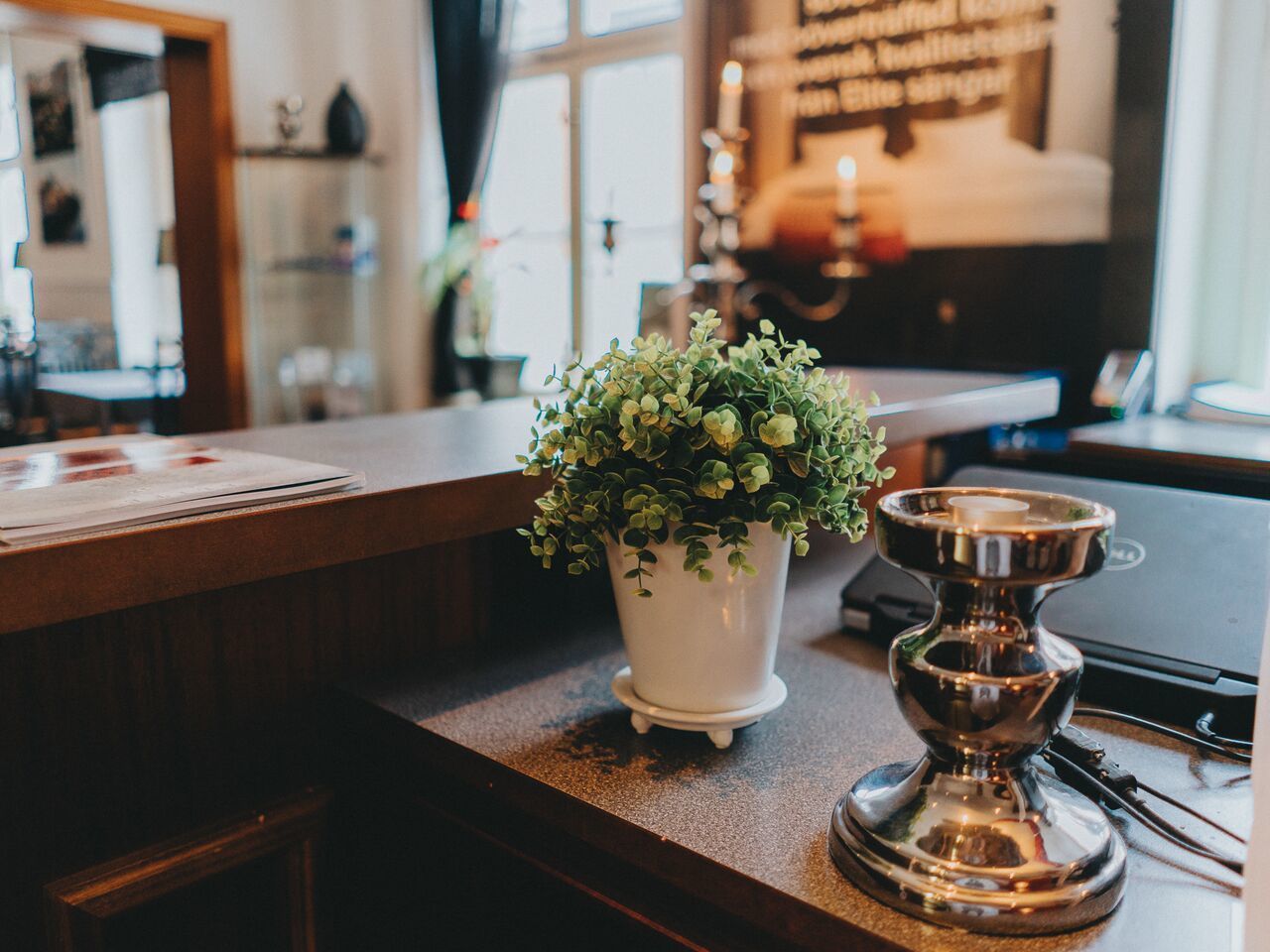 A wooden counter with a white pot of green plants and a silver candle holder.