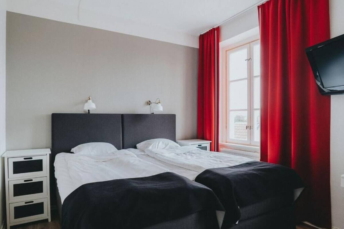 A double bed with white linens, a bedside table with a lamp, and a TV mounted on the wall.
