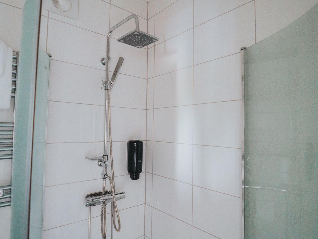 Un área de ducha con un cabezal de ducha de mano, un grifo empotrado en la pared y un dispensador de jabón.