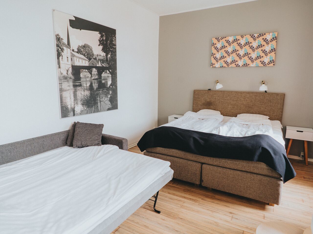 Un dormitorio con una cama, una cama más pequeña, una mesita de noche y una lámpara de pared.