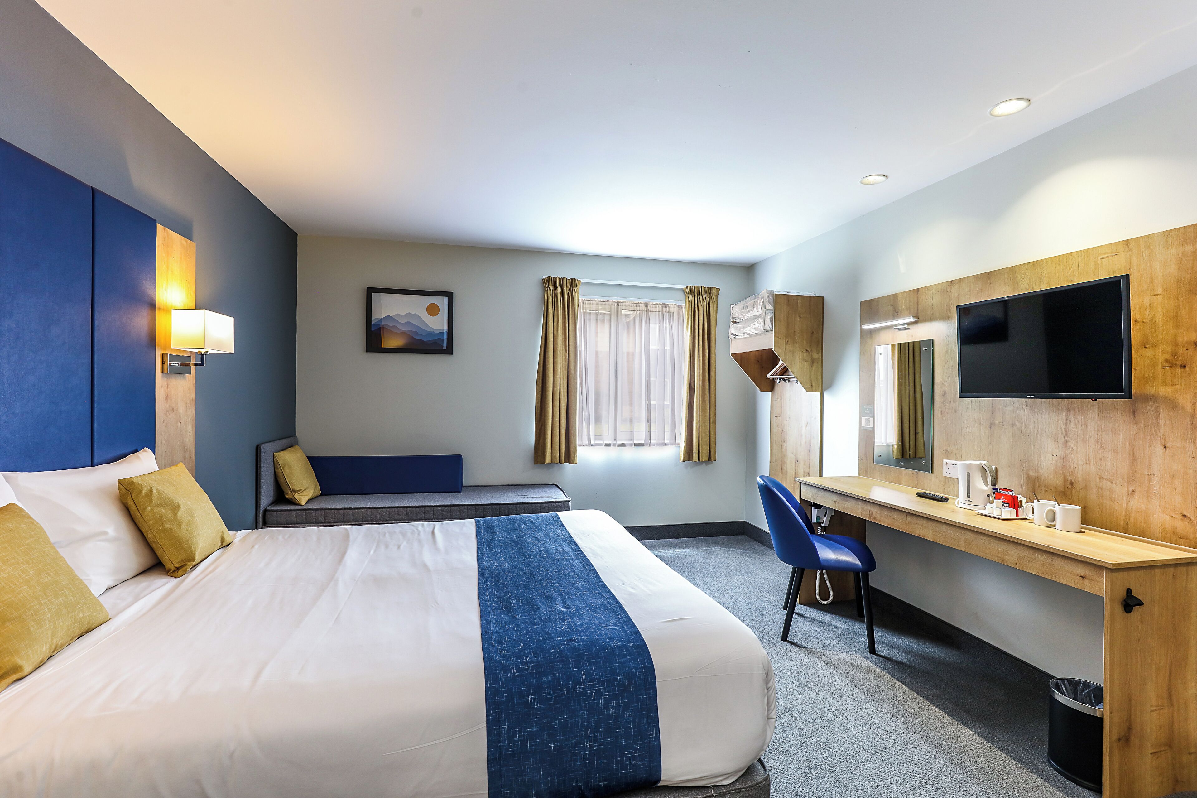Een hotelkamer met een bed, een bureau, een stoel, een televisie en een raam met gordijnen.