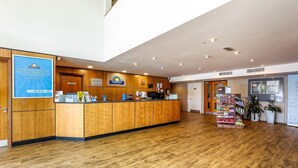 A reception desk with a Days Inn sign, a coffee machine, a small kiosk, and a plant. - Days Inn by Wyndham Peterborough (Peterborough)
