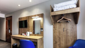 A hotel room with a wooden desk, a blue chair, a hanging coat rack, and a bed with a mattress. - Days Inn by Wyndham Peterborough (Peterborough)
