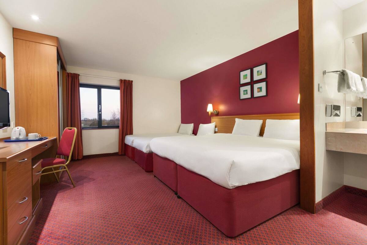 Habitación de hotel con una cama grande, un escritorio con computadora, una silla y un ventanal con cortinas.