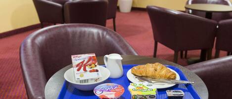 A breakfast tray with a croissant, yogurt, and juice on a hotel table.