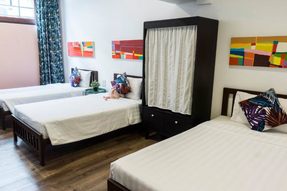 A hotel room with two single beds, a large wardrobe, and colorful artwork on the walls.