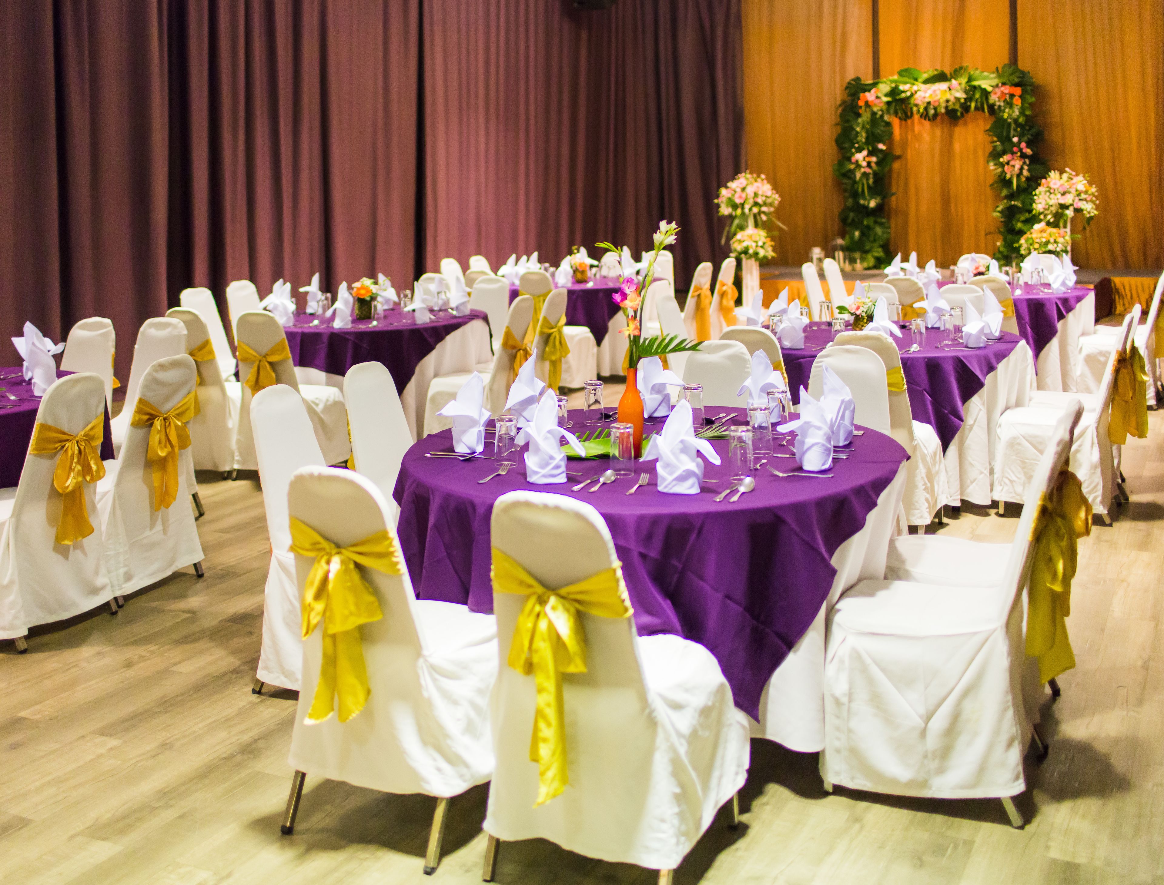 A banquet hall with round tables covered in purple tablecloths, white chairs with yellow sashes, and floral centerpieces.