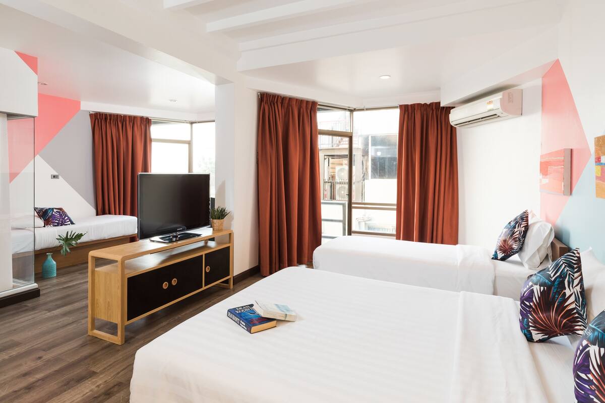 A hotel room with two beds, a TV, a wooden side table, and a window with curtains.