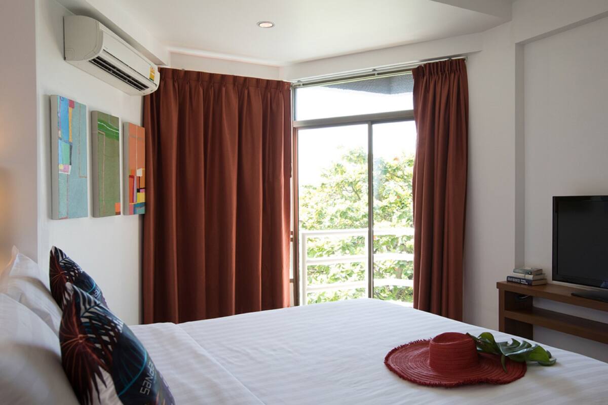 A hotel room with a large bed, a TV on a wooden stand, and a window with curtains.