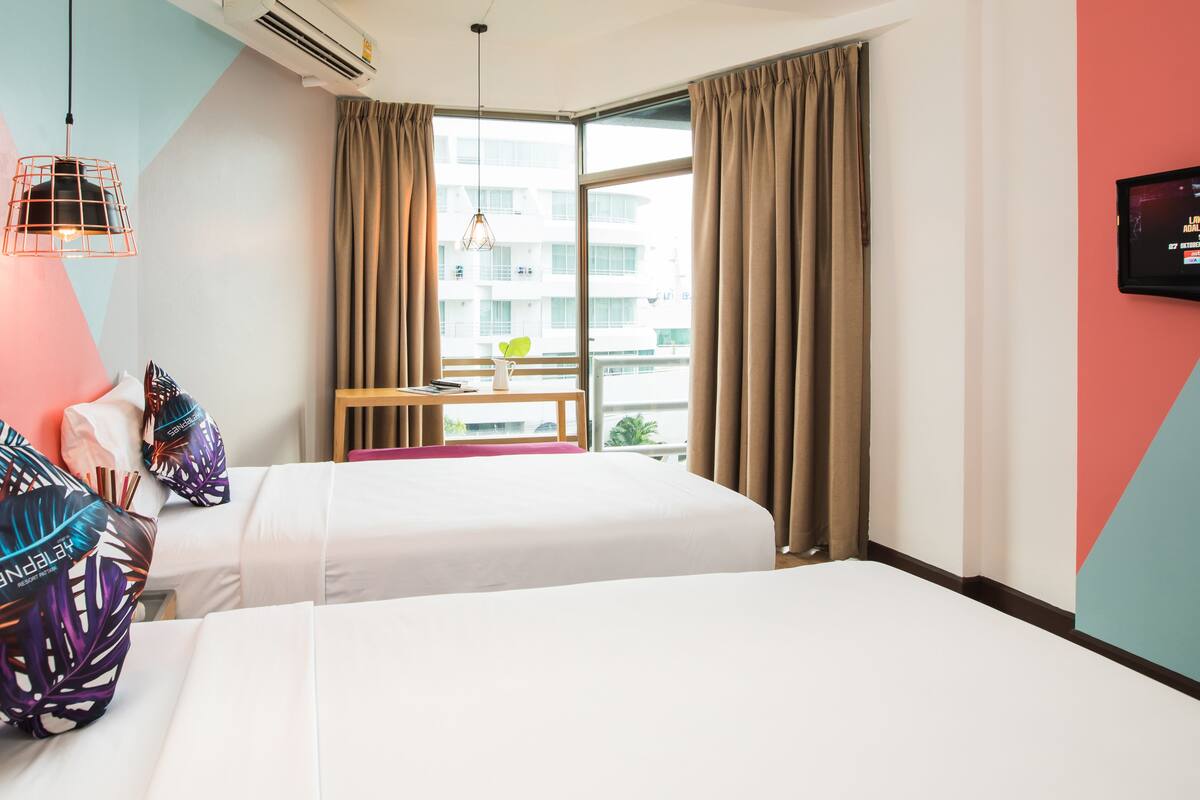 A hotel room with two beds, a small table with a plant, and a window with curtains.
