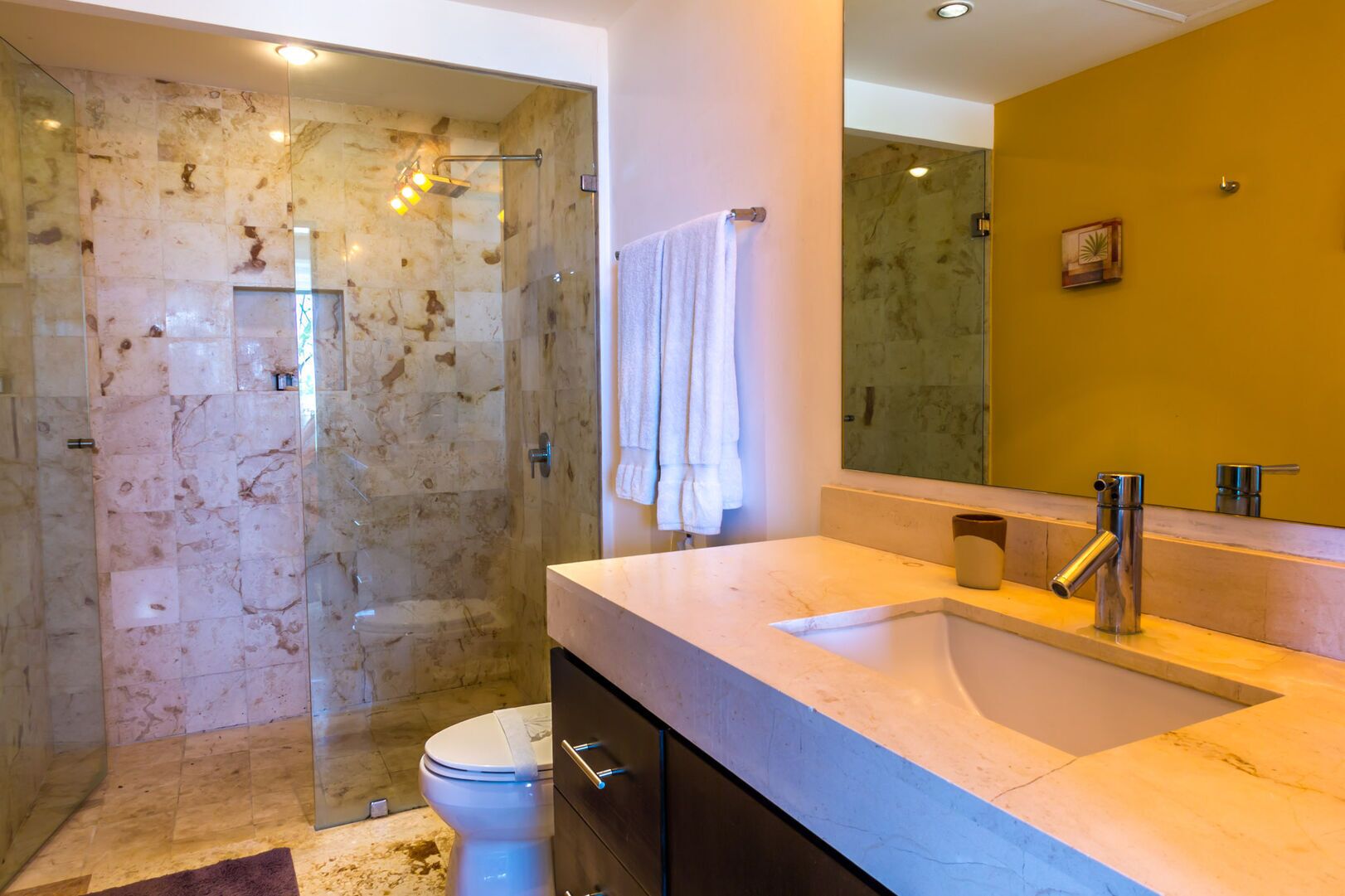 A modern bathroom with a glass-enclosed shower, a marble sink, and a large mirror.