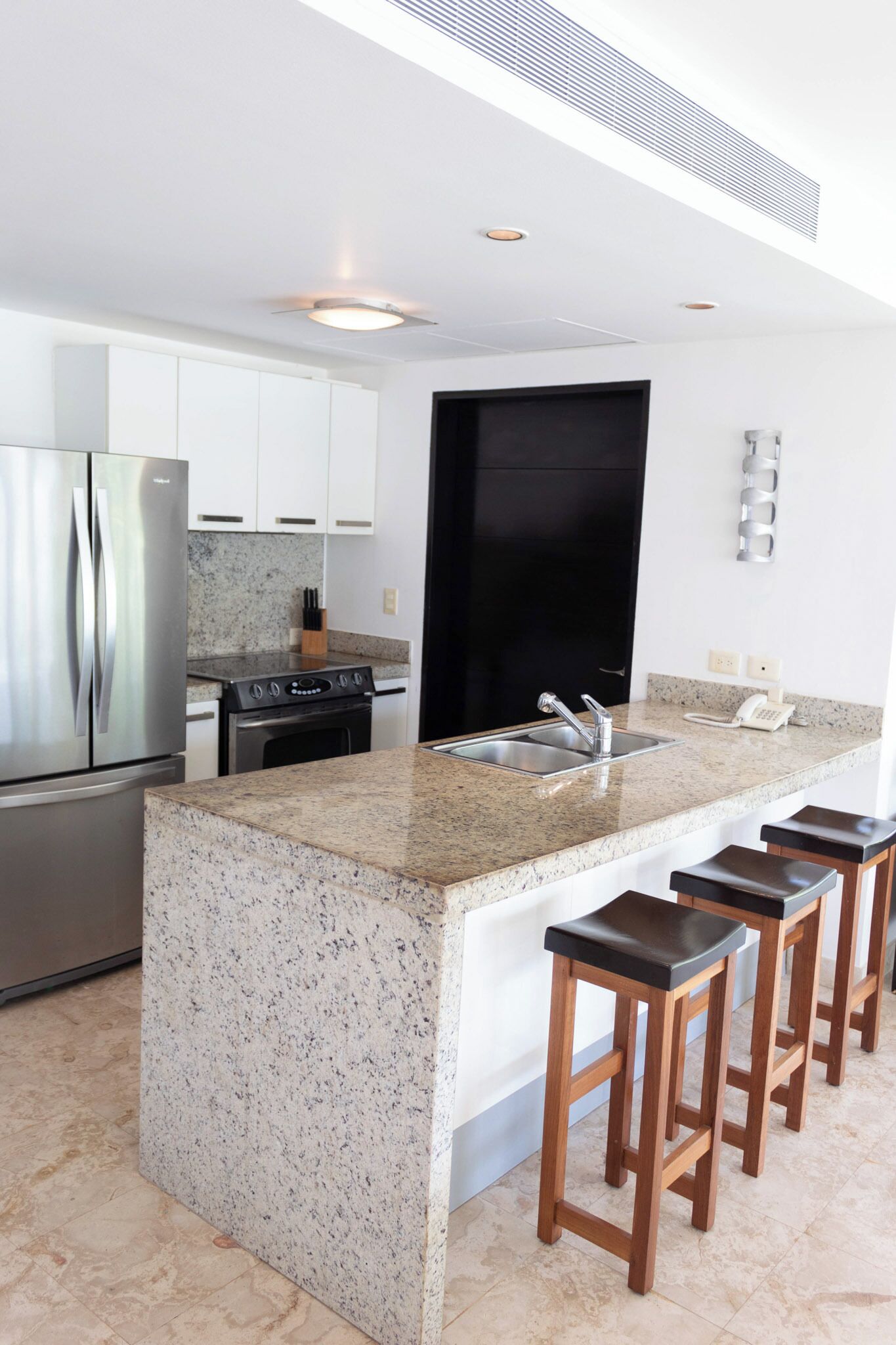 A modern kitchen with granite countertops, stainless steel appliances, and wooden bar stools.