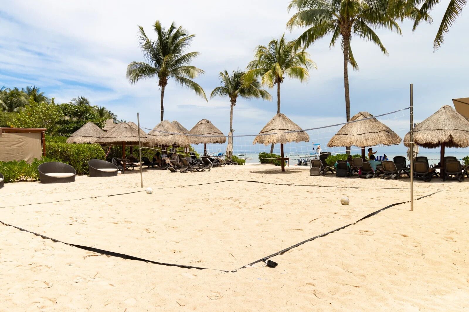 A beach volleyball court with thatched umbrellas and lounge chairs.