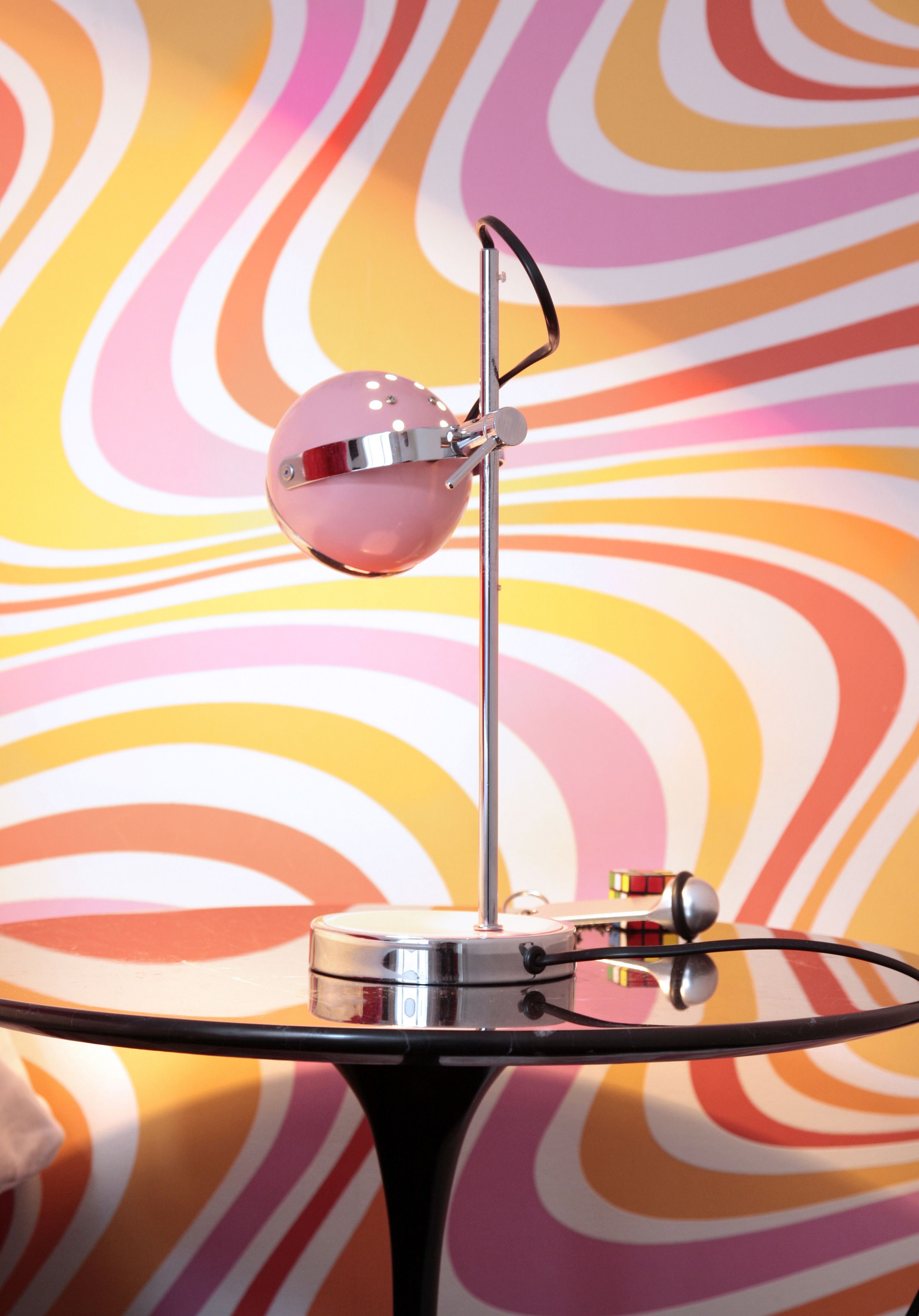 A table with a modern lamp and a colorful, abstract wall design in the background.
