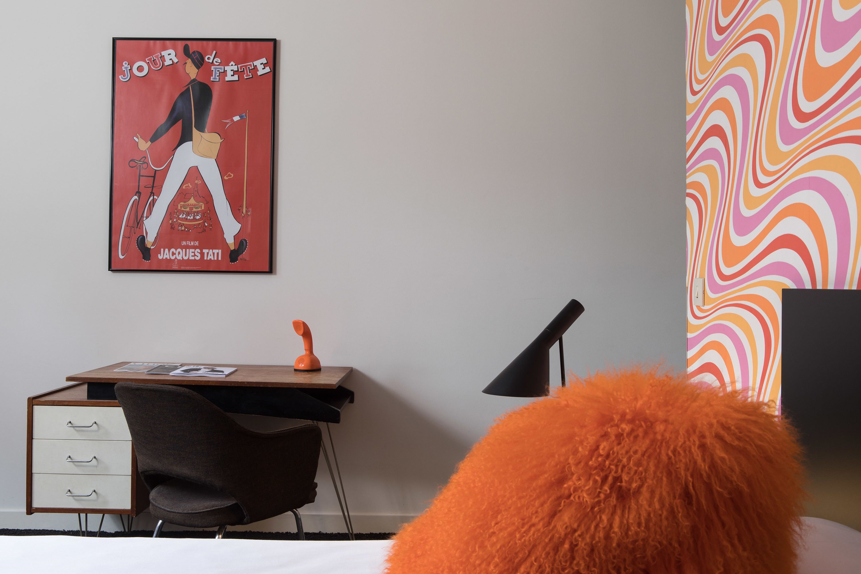 A bedroom with a bed, a desk with a chair, a poster on the wall, and a colorful wall design.