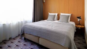 Habitación de hotel con cama, cortinas, pared de paneles de madera, una mesita con lámpara y piso estampado.