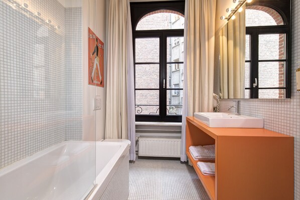 A bathroom with a bathtub, a sink, and a window with curtains.