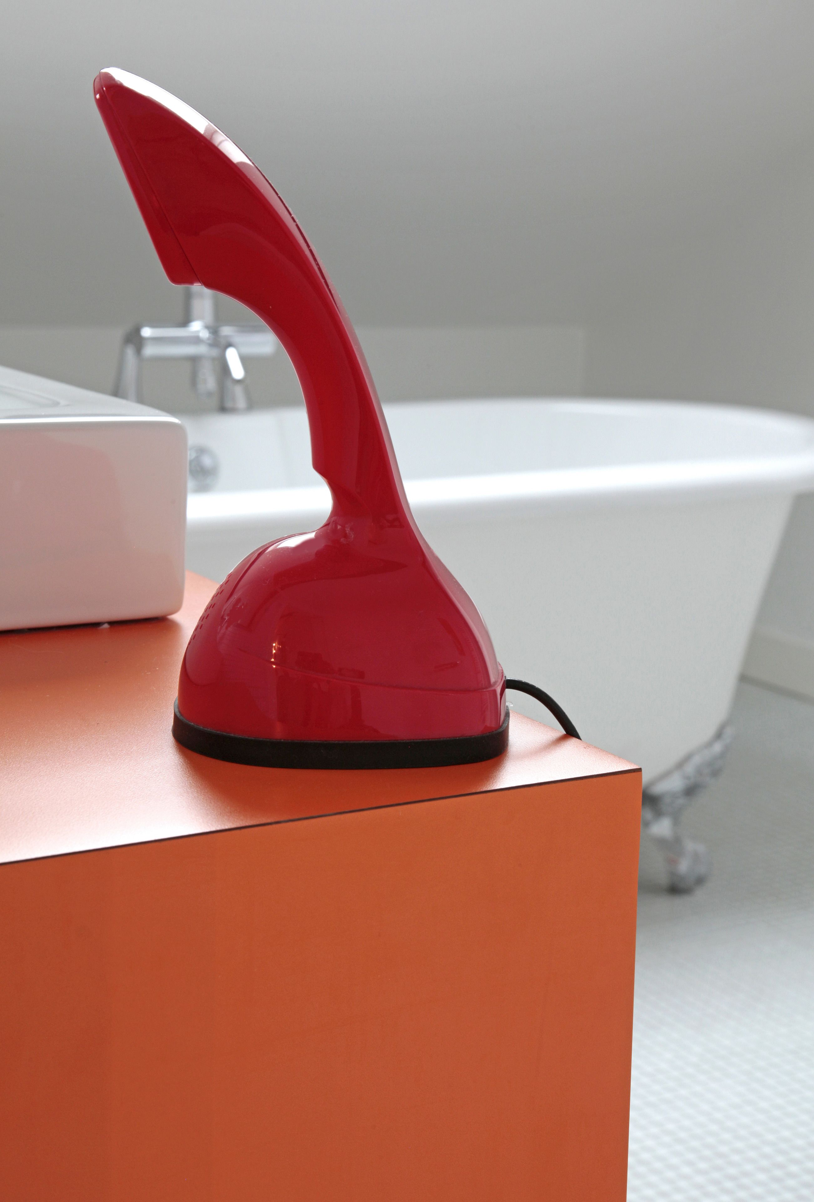 A red hair dryer on an orange box in a bathroom with a white bathtub in the background.