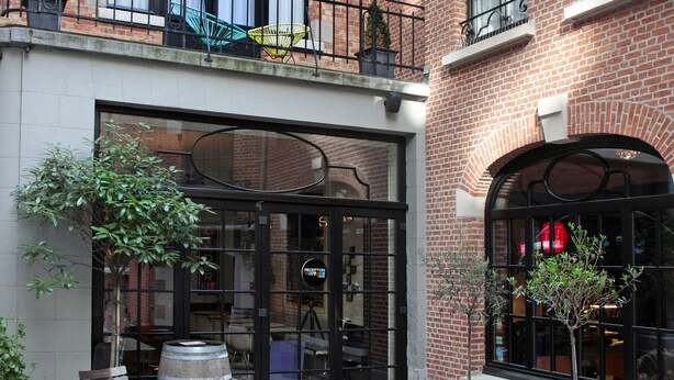 A courtyard with outdoor seating, potted plants, and a brick building with large windows.