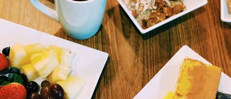 A breakfast table with various dishes including toast, fruit, scrambled eggs, bacon, and a cup of coffee.