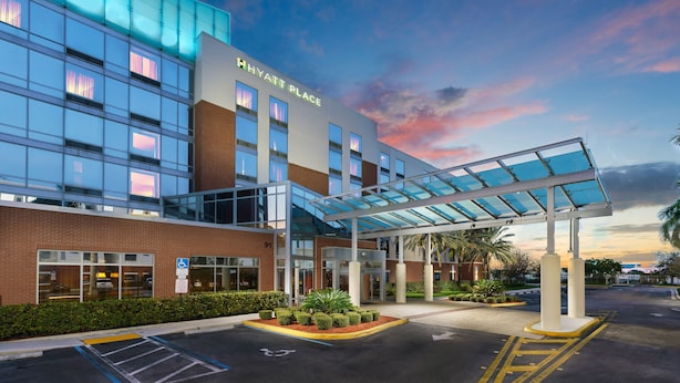 A modern hotel with a glass facade, a covered entrance, and a parking area. - Hyatt Place Ft. Lauderdale Airport & Cruise Port (Dania Beach)