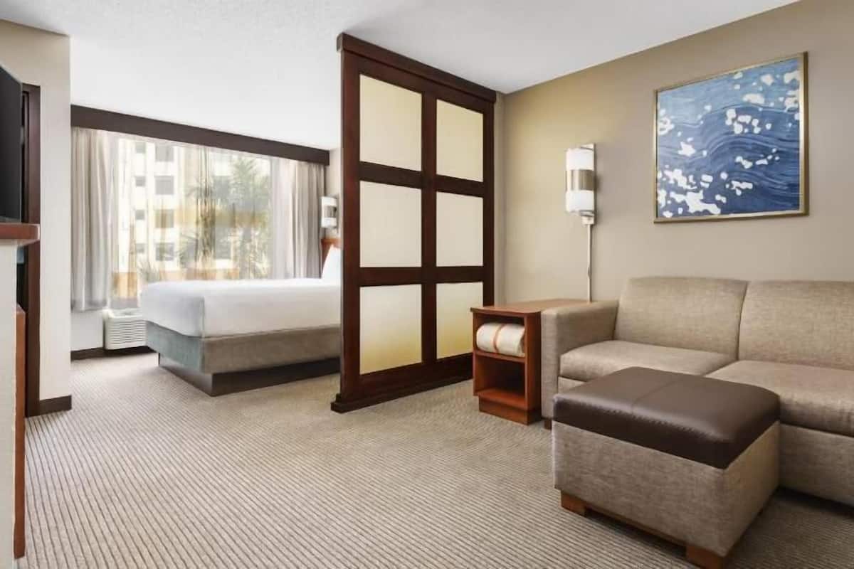 A hotel room with a bed, a sofa, a small table, and a painting on the wall.