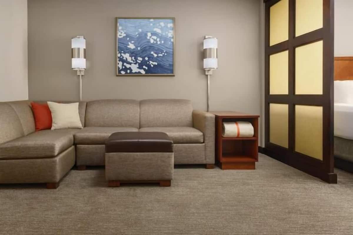 A L-shaped sectional sofa with a matching ottoman, a small wooden side table, and a wall-mounted floor lamp.