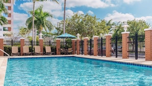 A swimming pool with lounge chairs and a fence, surrounded by palm trees and a building. - Hyatt Place Ft. Lauderdale Airport & Cruise Port (Dania Beach)