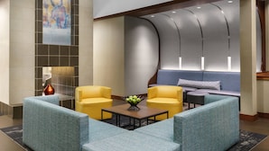 A lobby with a seating area featuring blue and yellow chairs, a coffee table with a fruit centerpiece, and a large abstract painting on the wall. - Hyatt Place Ft. Lauderdale Airport & Cruise Port (Dania Beach)