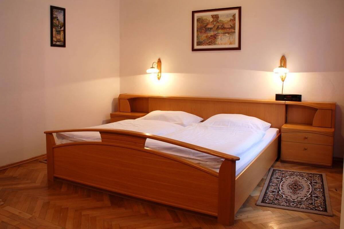 Un lit en bois avec du linge de lit blanc, une table de chevet et une lampe de chevet, ainsi que deux lampes fixées au mur.