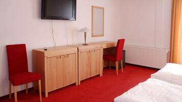 Una camera d'albergo con un letto, una scrivania con una sedia, una televisione e un termosifone.