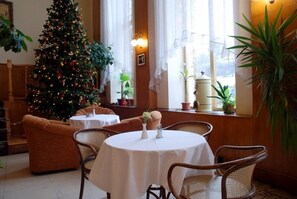 A cozy dining area with a Christmas tree, wicker chairs, and a table with a vase. - Hotel Grand Matej (Banska Stiavnica)