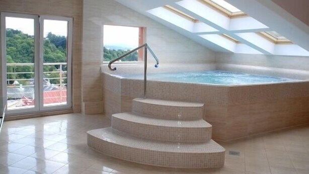 Ein Whirlpool mit einer Treppe, die hinaufführt, einem Dachfenster darüber und Blick auf Grünfläche.