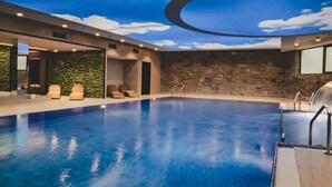 A modern indoor swimming pool with a stone wall and a ceiling simulating a blue sky with clouds. - Hotel Crocus (Zakopane)