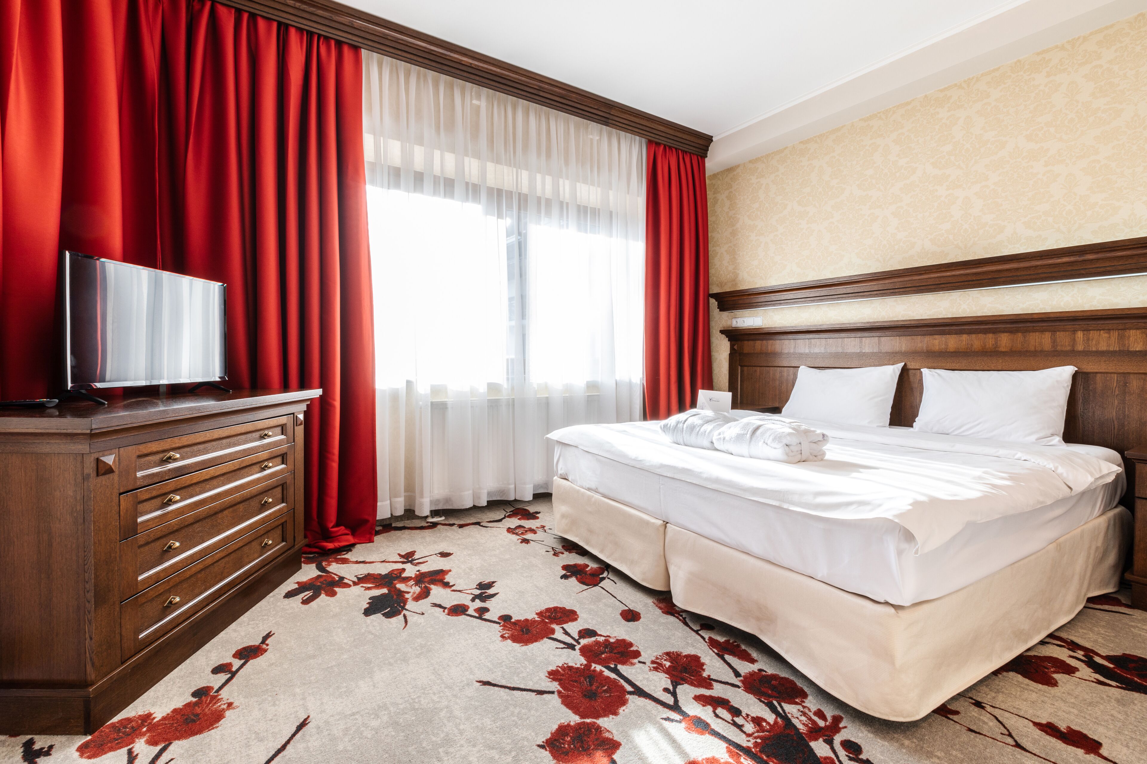 Una camera d'albergo con un letto, una cassettiera, una televisione e una finestra con tende rosse.