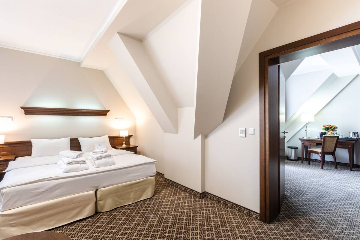 Ein Hotelzimmer mit einem großen Bett, einem Schreibtisch und einem Sessel. Es gibt ein Fenster mit Blick nach draußen.