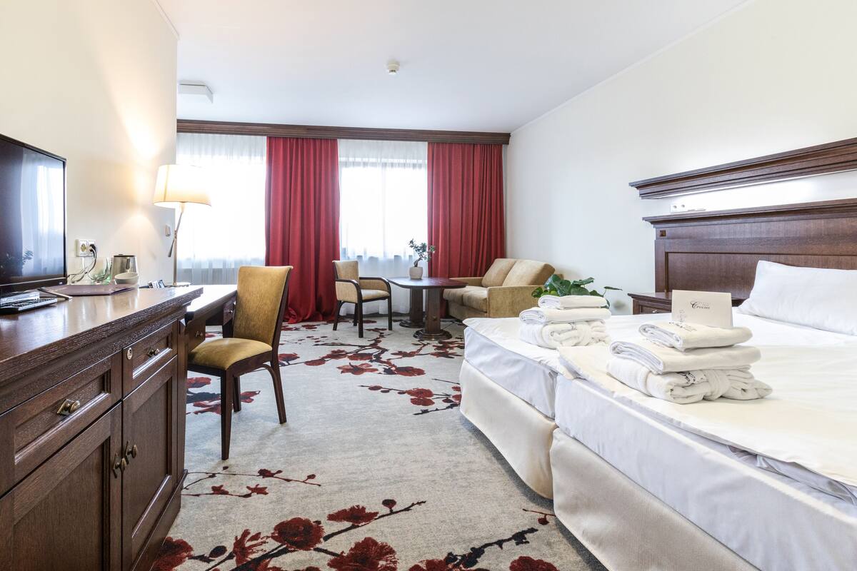 Ein Hotelzimmer mit Bett, Schreibtisch, Sessel, Fernseher und einem Fenster mit Vorhängen.