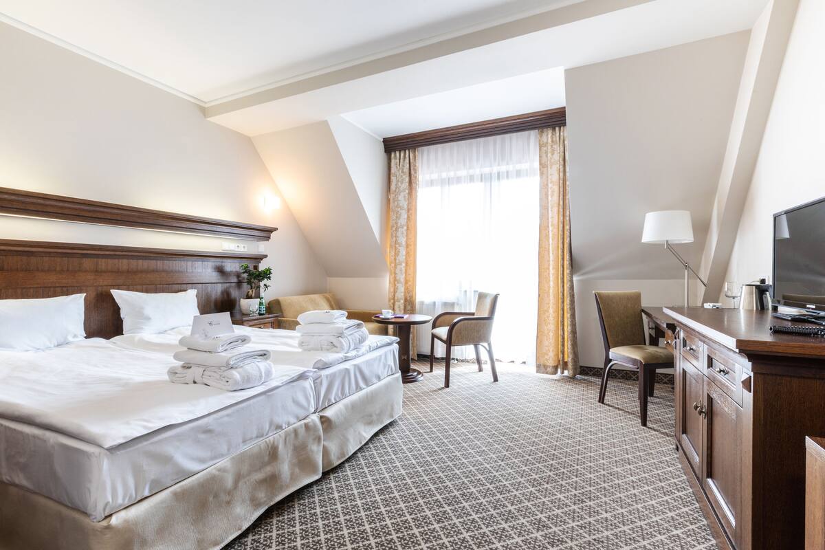 Ein Hotelzimmer mit einem großen Bett, einem Schreibtisch, einem Sessel, einem Fernseher und einem Fenster mit Vorhängen.