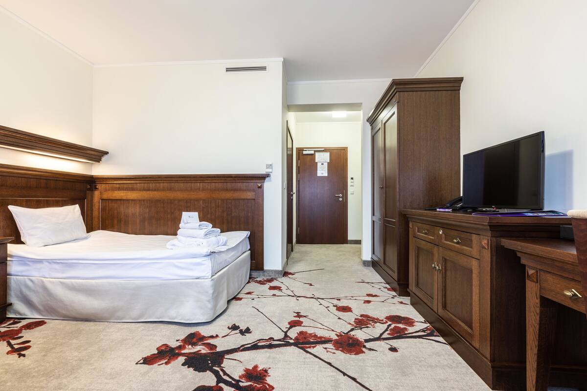 Ein Hotelzimmer mit einem Bett, einem Fernseher, einer Holzkommode und einem Teppich mit floralem Muster.
